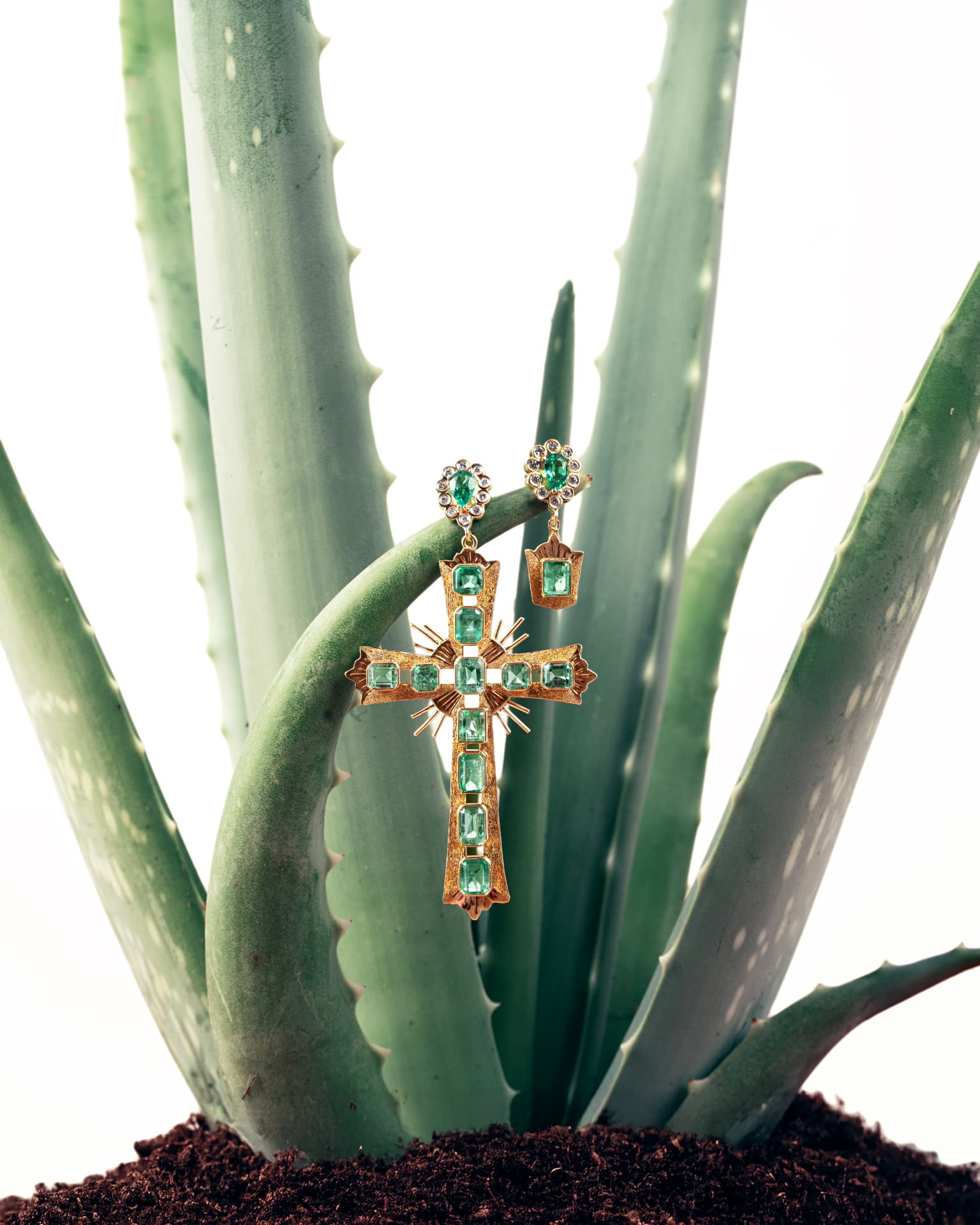 Cruz y pendientes con piedras verdes sobre una planta de aloe